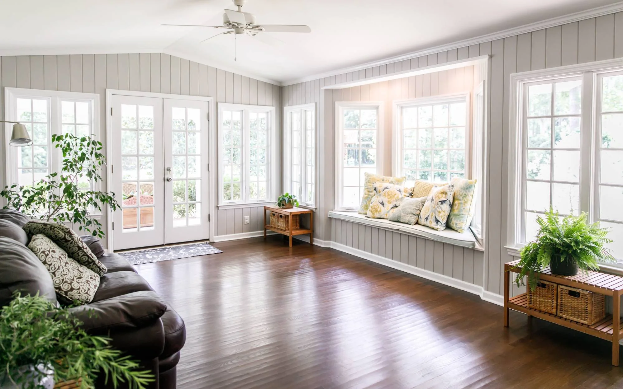 A bright sun room with a comfortable couch, a chair, and a window that offers a view of the outdoors.