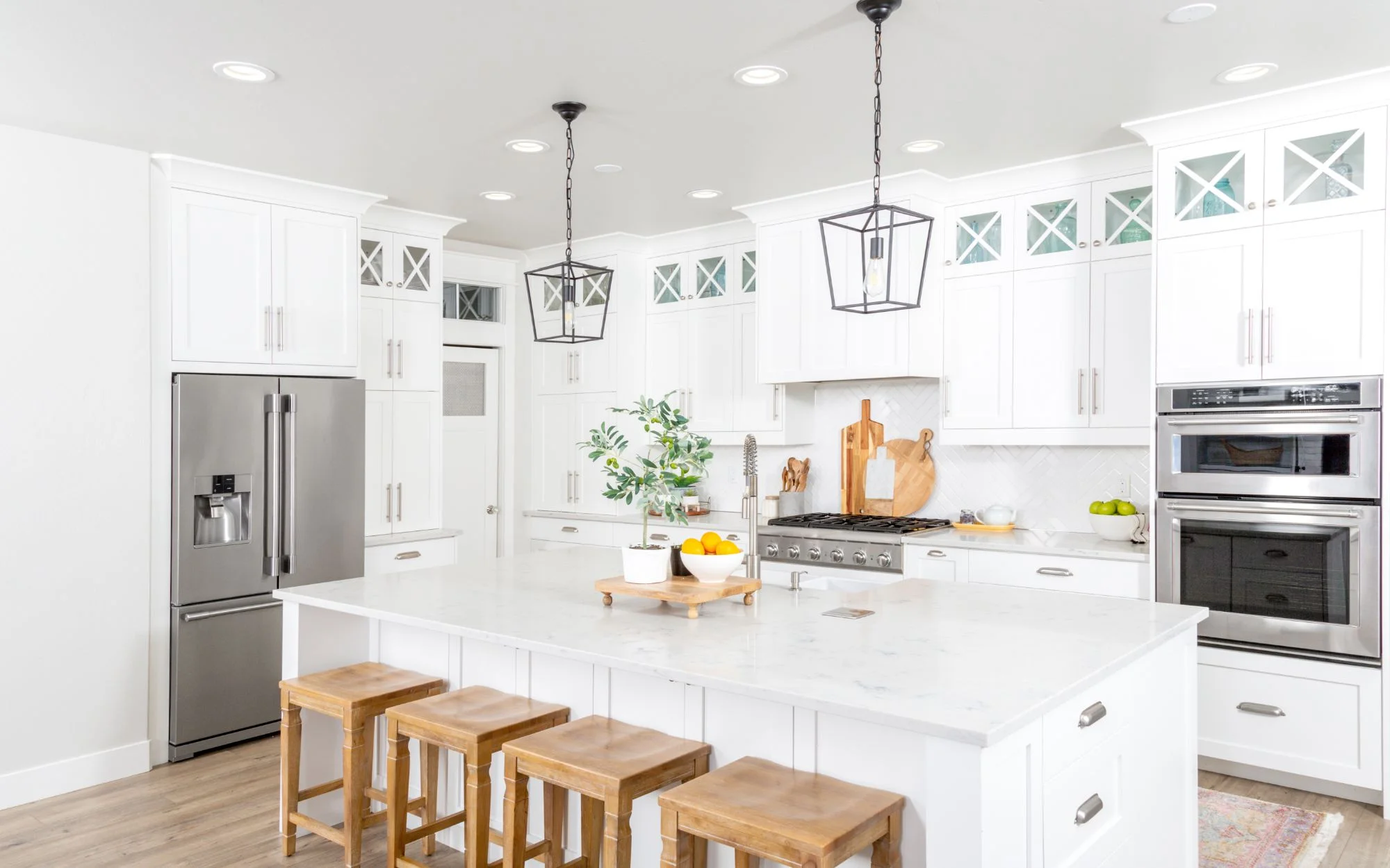A bright white kitchen featuring a central island and wooden stools for seating.