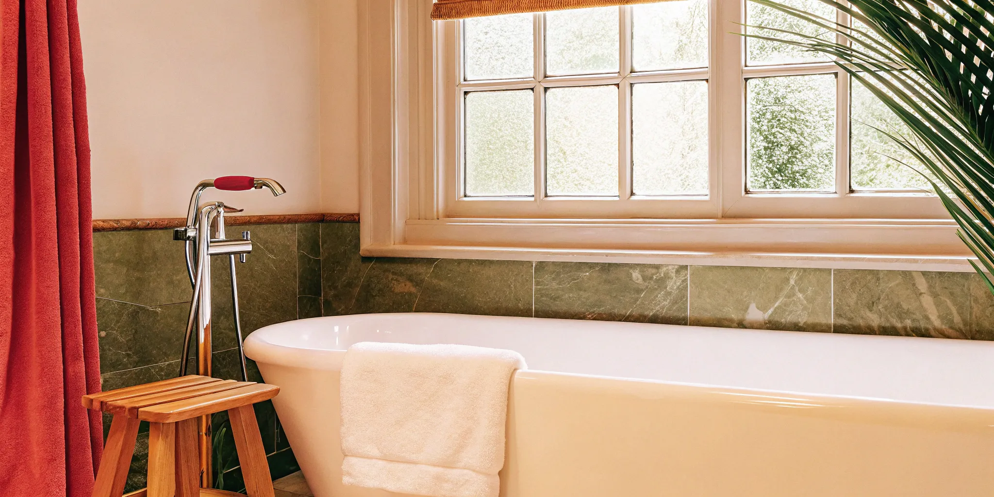 Spa-like master bathroom renovation with a freestanding tub, green tile, and natural light from a large window.